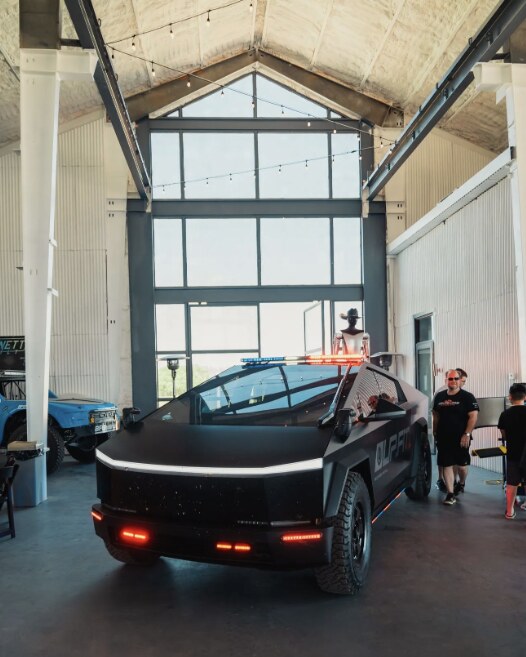 A matte black Tesla Cybertruck with a light bar parked inside a high-ceilinged venue at the Cybertruck Rodeo